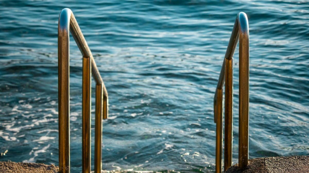 Close-up of stainless steel pool handrails leading to a calm ocean view.