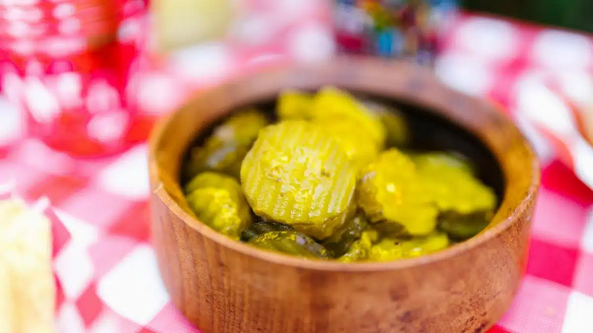 Close-up of pickled cucumbers in a wooden bowl on a red and white checked tablecloth, perfect for food photography.