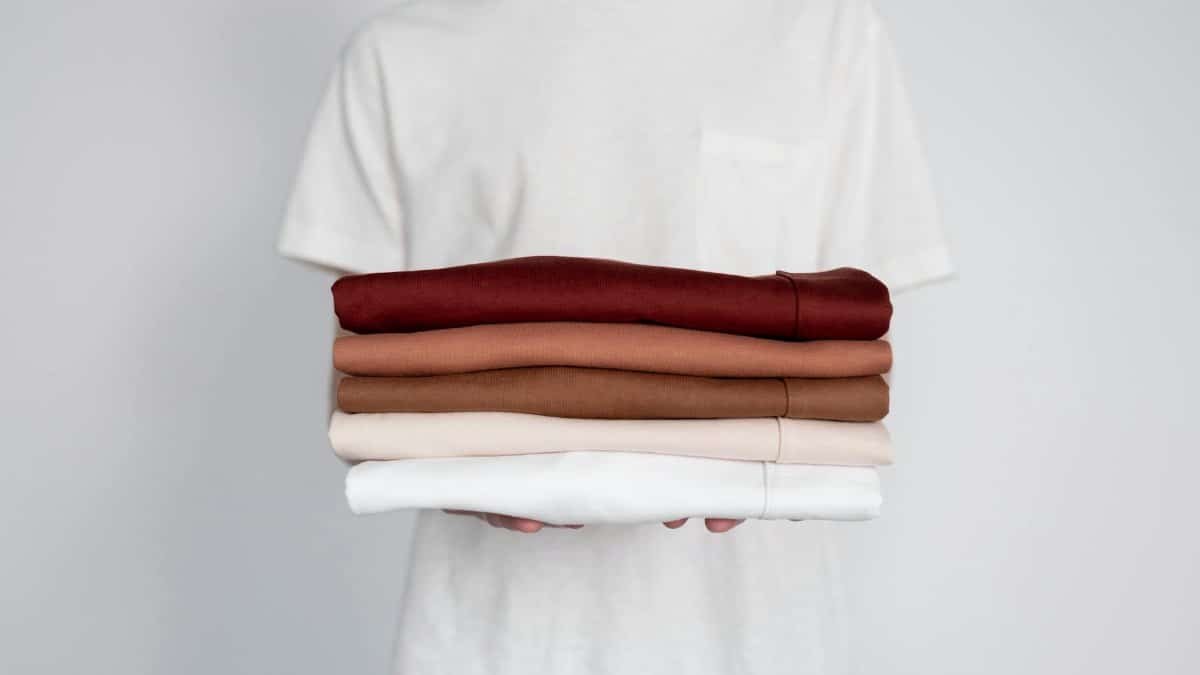 Minimalist close-up of folded neutral-colored shirts held by a person.