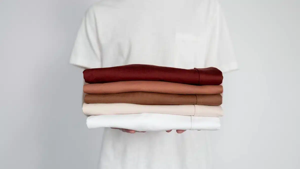 Minimalist close-up of folded neutral-colored shirts held by a person.