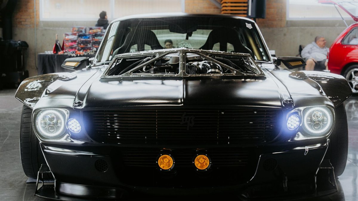Front view of a sleek, modified black muscle car in an indoor showroom setting.