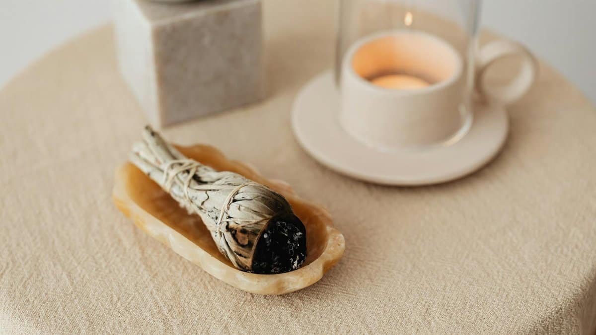 A peaceful aromatherapy scene featuring a burning candle and sage on a beige tablecloth.