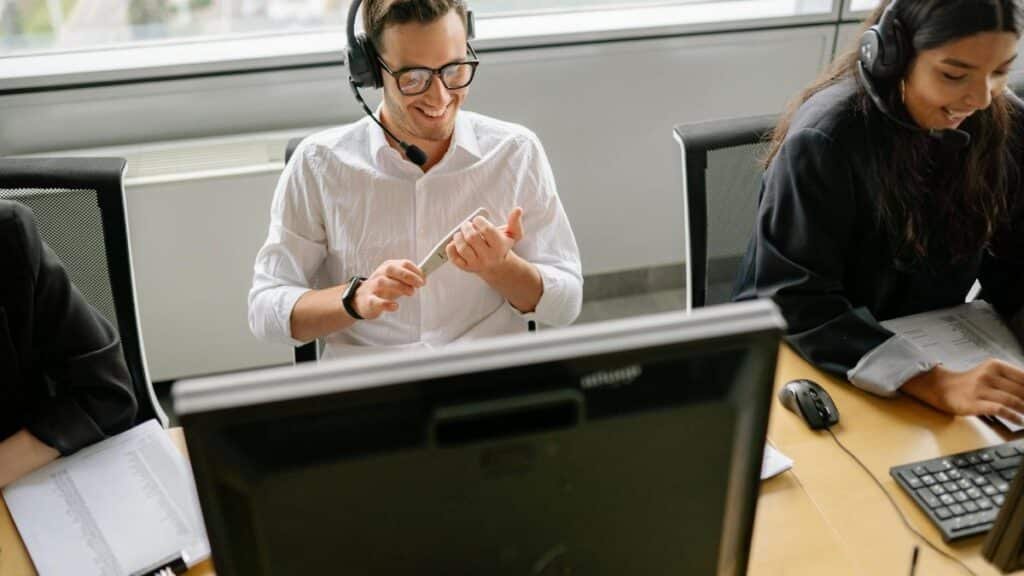 Colleagues working at a desk with computers and headsets in a modern office setting.
