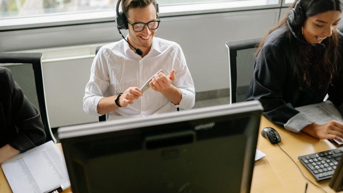 Colleagues working at a desk with computers and headsets in a modern office setting.