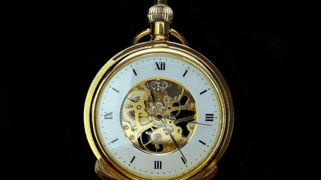 Detailed close-up of a vintage gold mechanical pocket watch on a black background, showcasing gears and roman numerals.