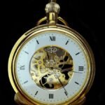 Detailed close-up of a vintage gold mechanical pocket watch on a black background, showcasing gears and roman numerals.