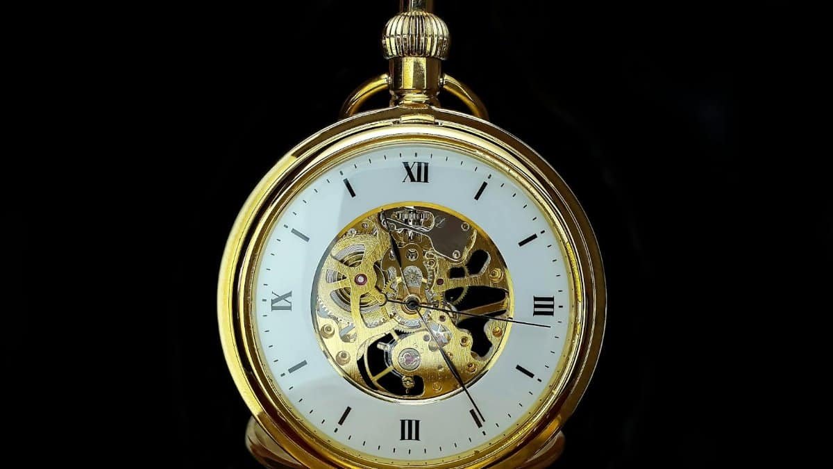 Detailed close-up of a vintage gold mechanical pocket watch on a black background, showcasing gears and roman numerals.