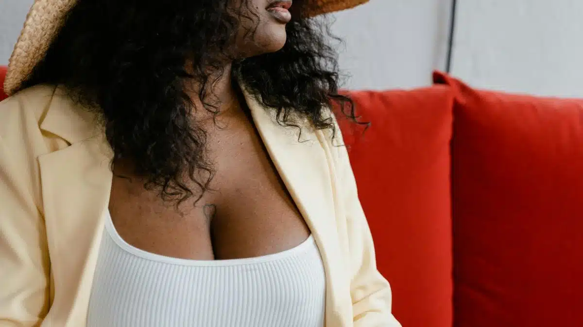 Fashionable woman wearing a hat and jacket seated on a vibrant red sofa.
