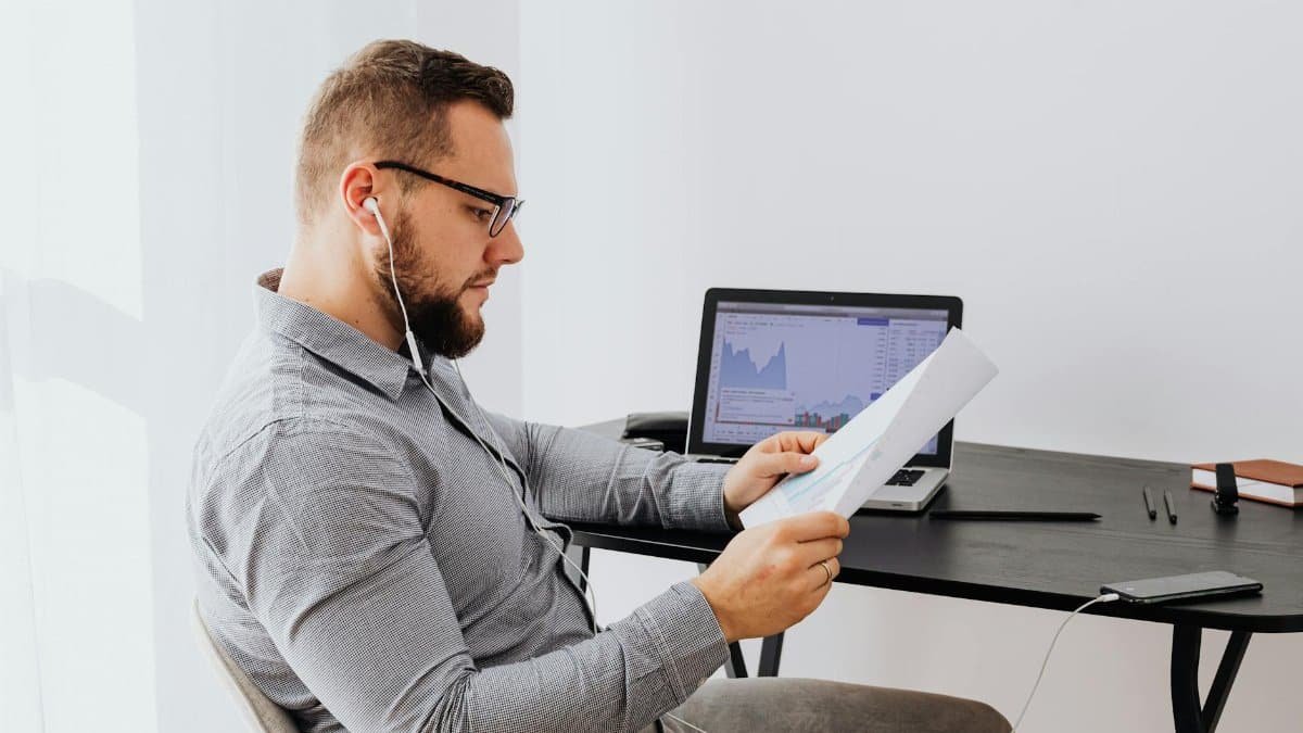 Professional analyzing financial charts on laptop and paperwork in an office setting.