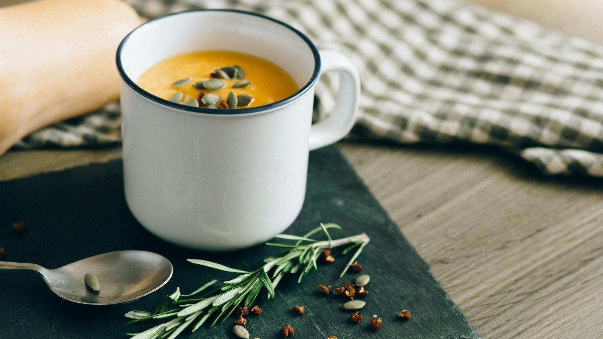 Warm pumpkin soup garnished with seeds and herbs in an enamel mug, perfect for fall comfort food.