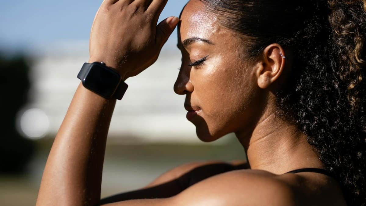 Side profile of a woman meditating outdoors in sunlight, wearing a smartwatch.