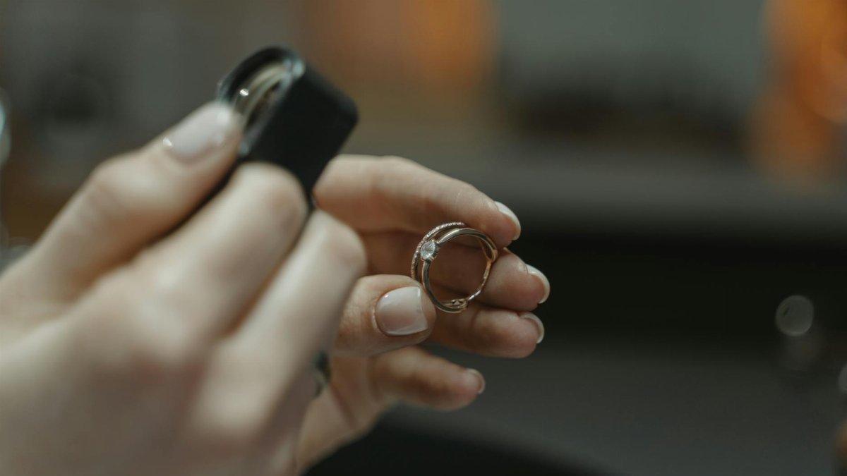 Close-up of a jeweler's hands holding a diamond ring and magnifying glass.