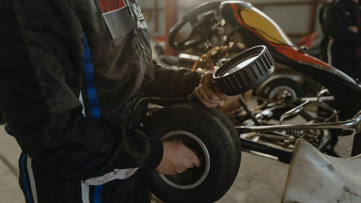 Mechanic working on a kart tire in an indoor garage setting, showcasing racing preparation.