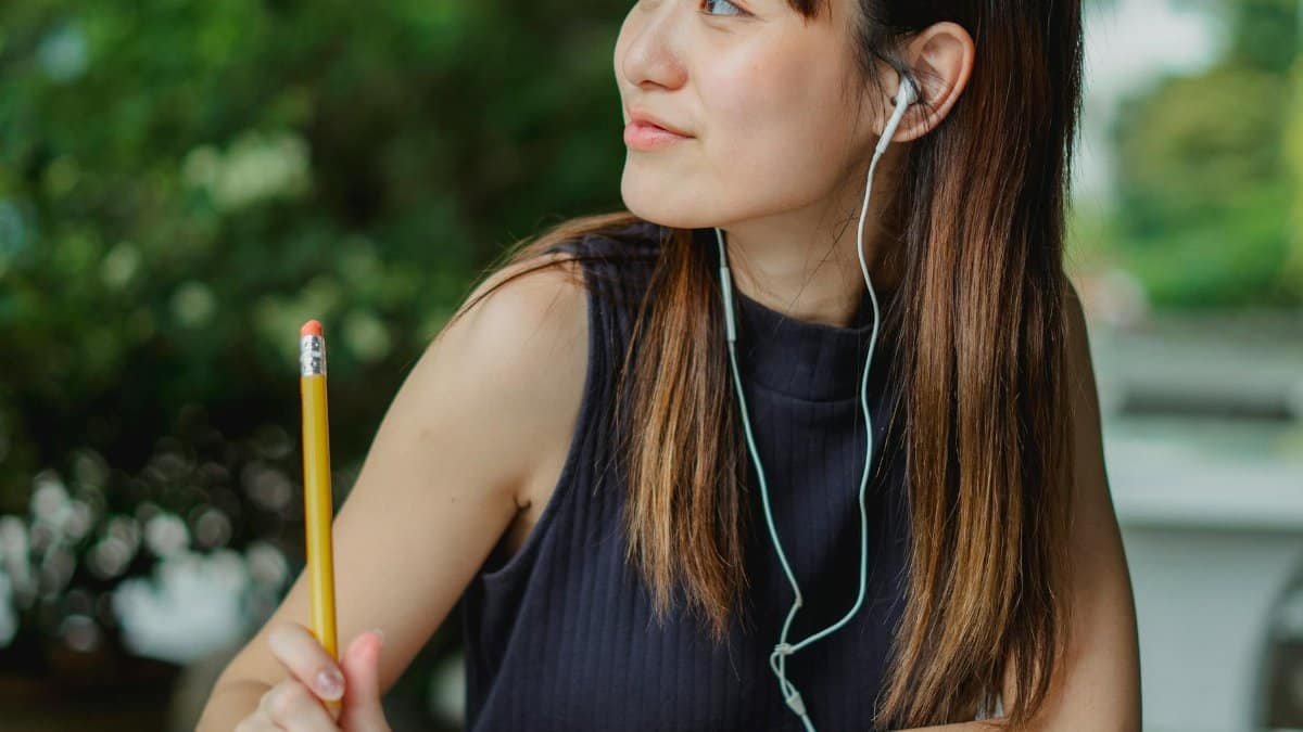 Asian woman smiling while listening to music with earbuds outdoors.