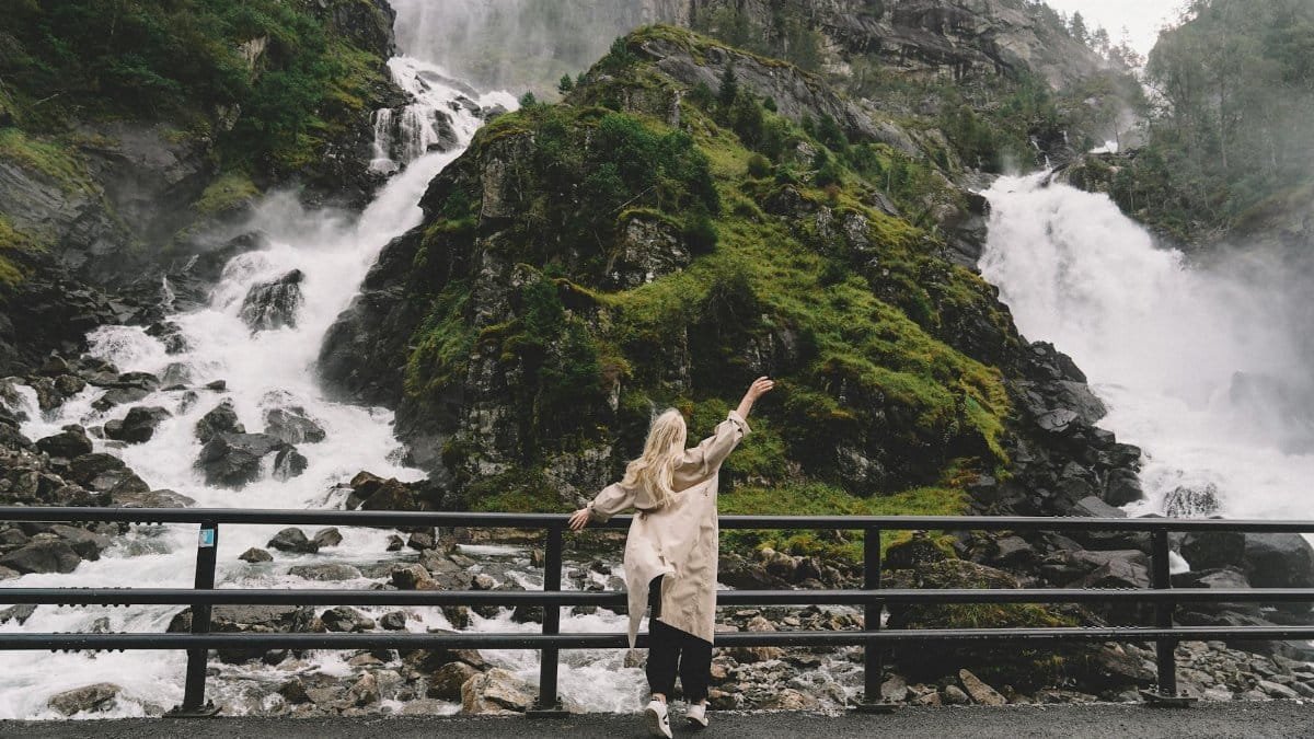 A woman enjoys a breathtaking view of a cascading waterfall amidst lush greenery.