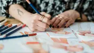 Crop anonymous tattooed female designer coloring apparel illustration on human figure on paper sheet while working at desk