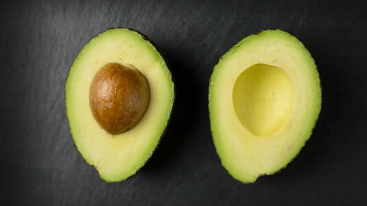 Close-up of fresh sliced avocado halves on a dark slate surface, showcasing healthy eating.