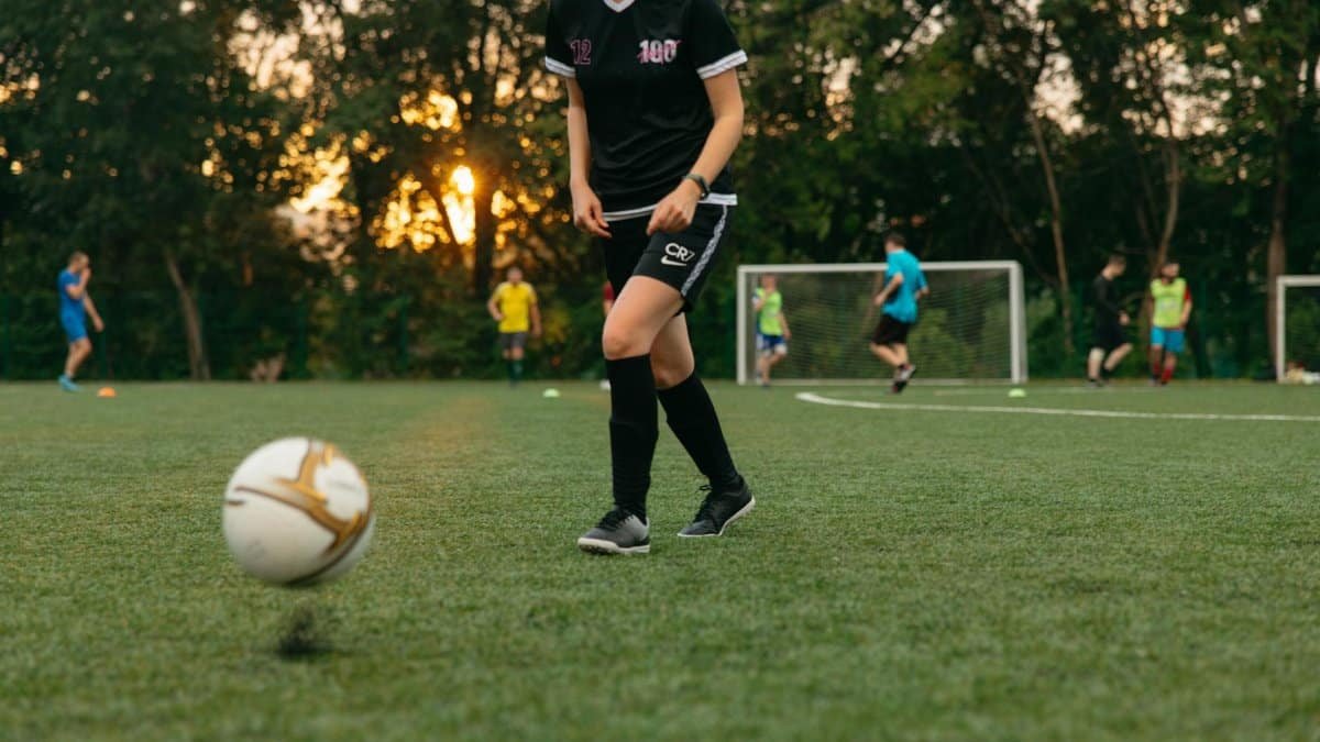 Female soccer player dribbling a ball during a casual game on a grassy field at sunset.