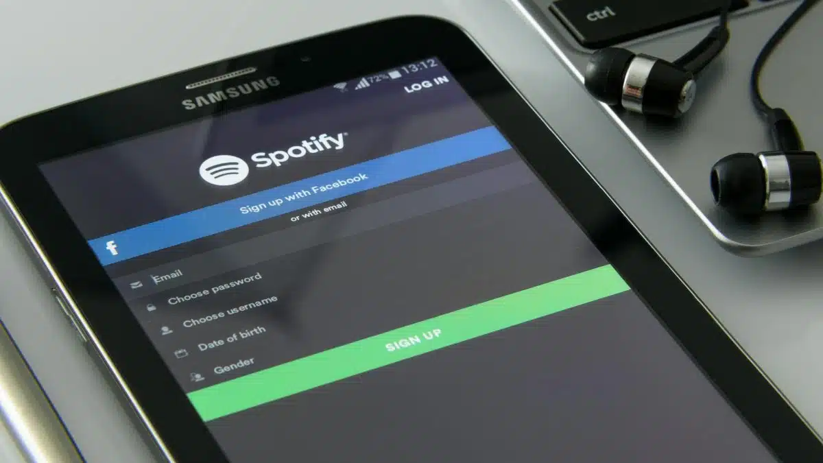 Smartphone showcasing Spotify login screen beside laptop and earphones on desk.