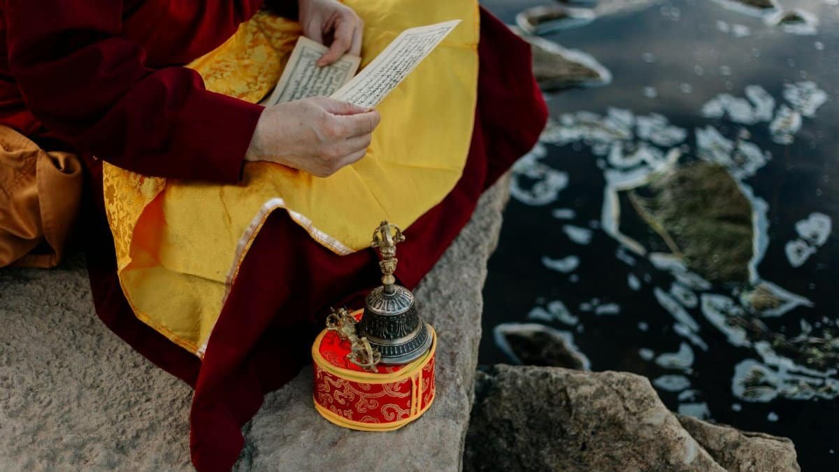 A Buddhist monk meditating with ritual items by a peaceful riverside, embracing spiritual practice.