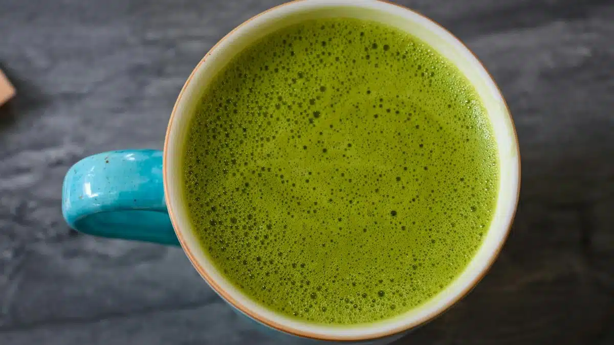 A top view of a ceramic cup filled with frothy green matcha latte on a dark surface.