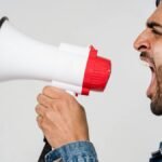 Close-up side view of a man shouting passionately into a megaphone, expressing urgency.