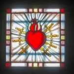 Vibrant stained glass depicting Sacred Heart in a church setting, symbolizing love and devotion.