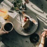 Overhead view of a cozy café table with a slice of cake, coffee, and juice, bathed in warm afternoon light.