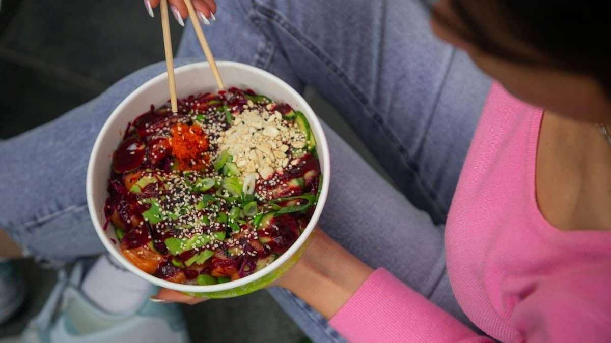 Vibrant poke bowl with vegetables and grains, held in hands, viewed from above.