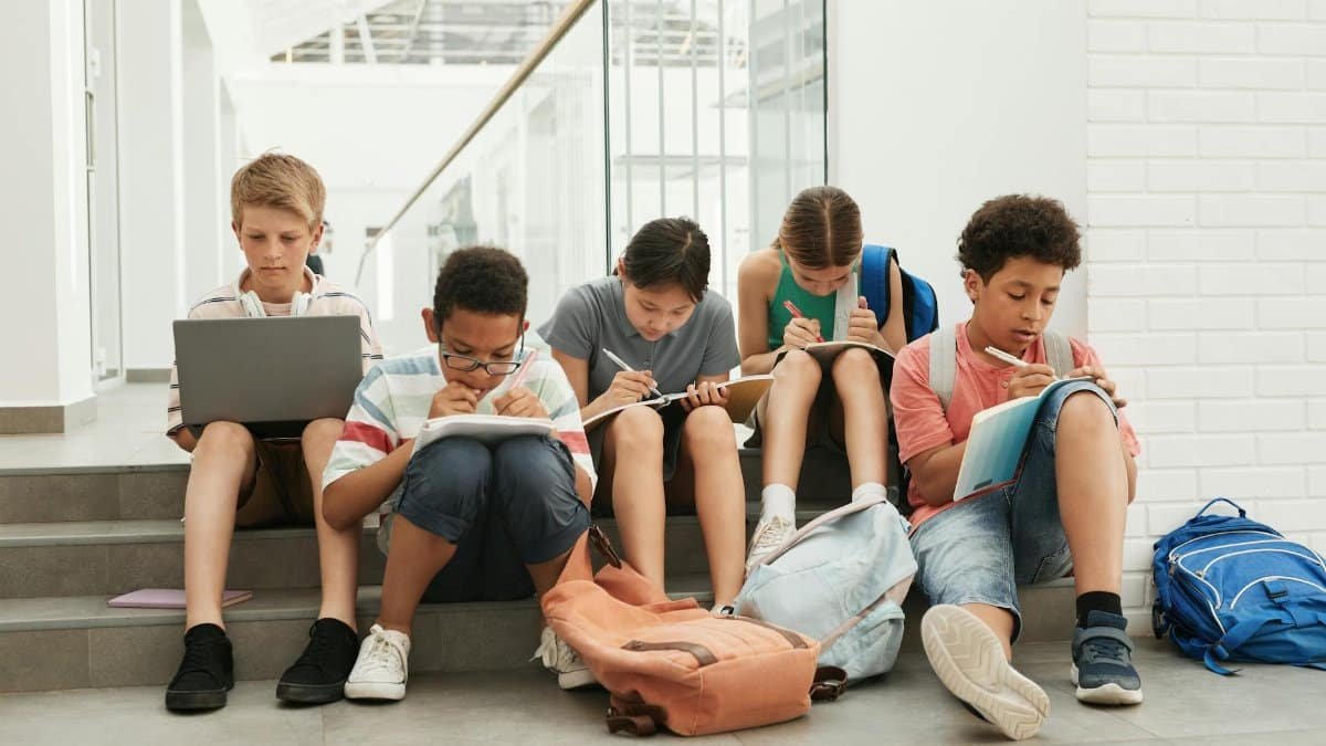 A group of school students sitting in a hallway, focused on studying and writing.