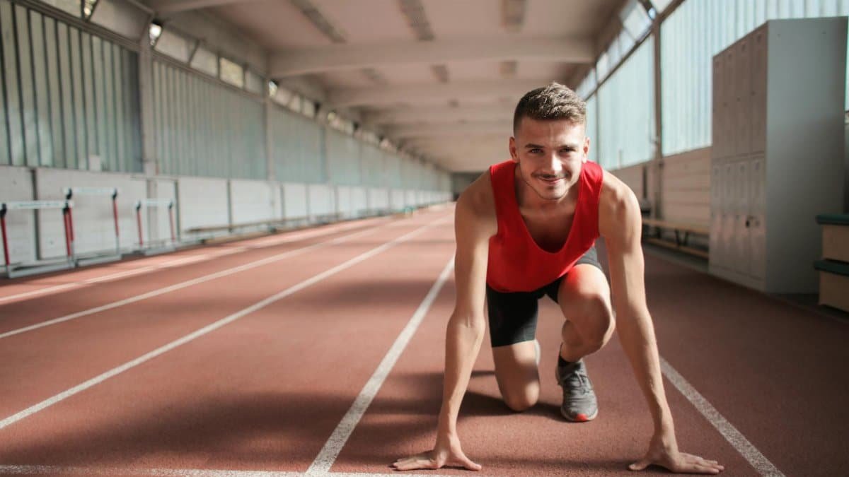 Male athlete in red top preparing for a sprint on an indoor track, showcasing determination and focus.