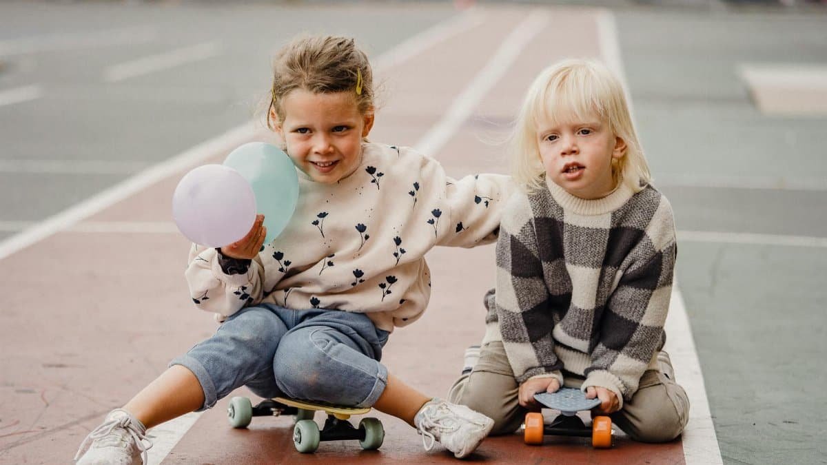 Two children enjoying time outdoors at a skate park with skateboards and balloons.