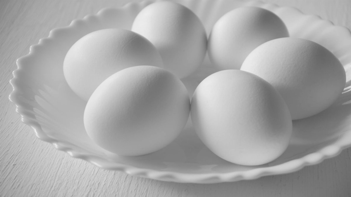 A close-up monochrome image of five eggs on a white plate, emphasizing texture and simplicity.