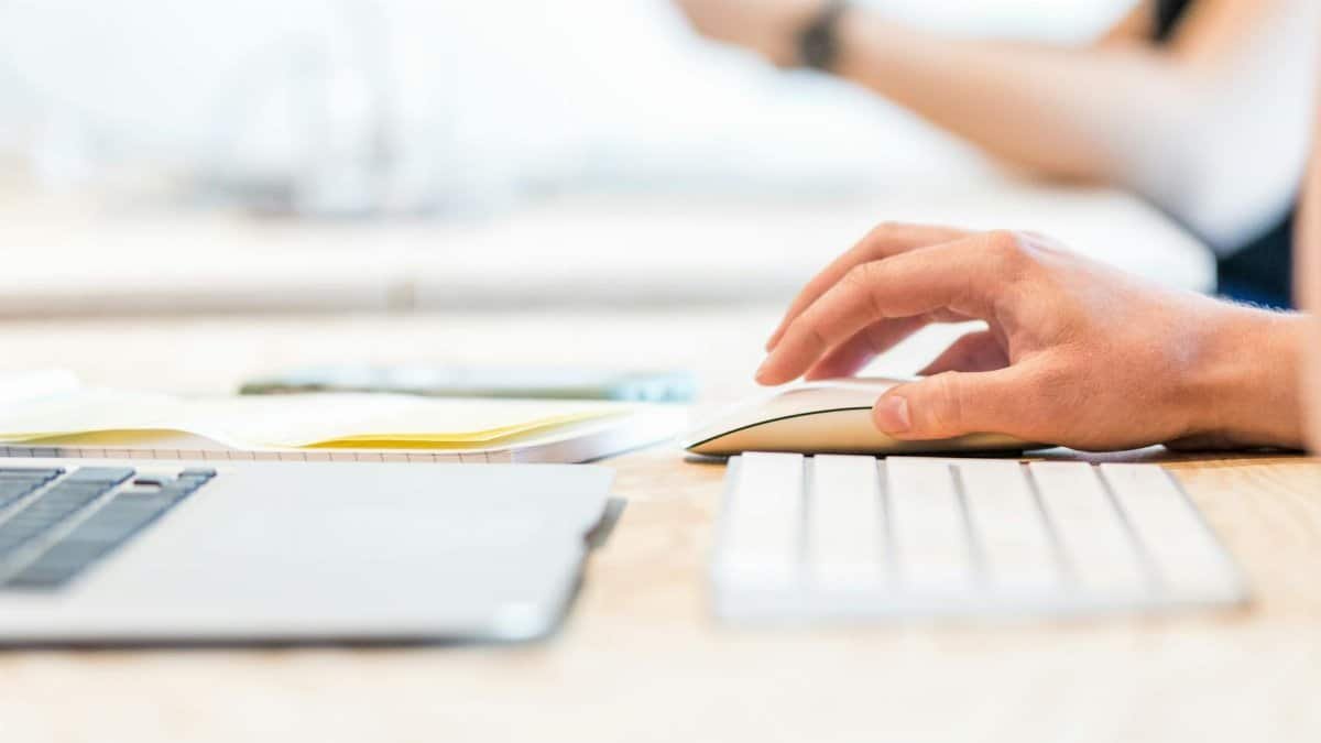 A person working at a laptop with a wireless mouse and keyboard in a bright office setting.