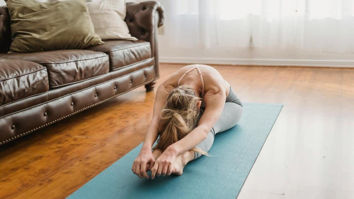 Woman doing yoga in a living room, focusing on a seated forward bend pose for wellness.
