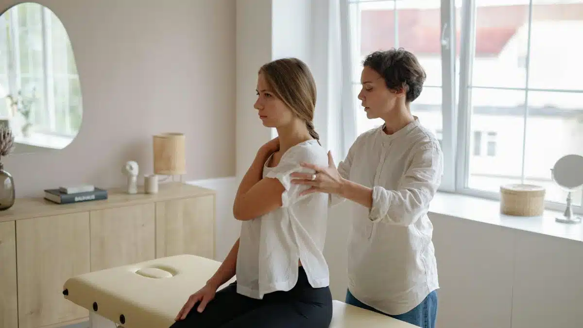 A massage therapist providing shoulder treatment to a woman in a well-lit studio.