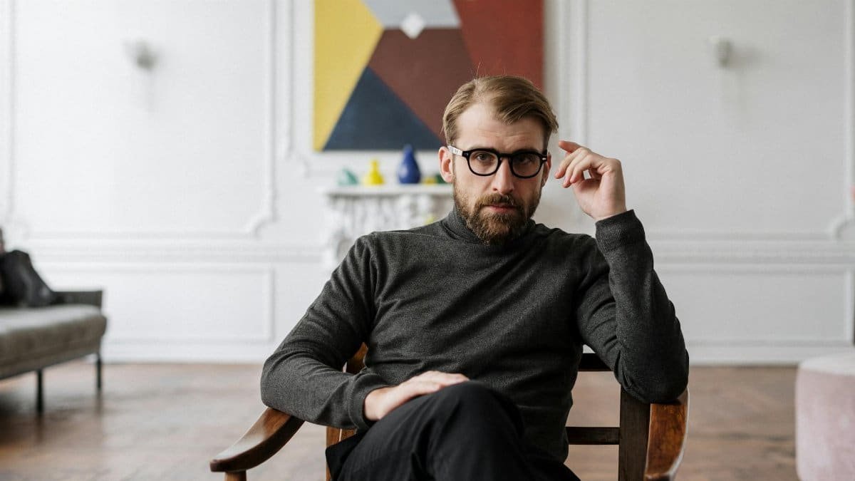 Man with glasses seated in modern interior with abstract art.