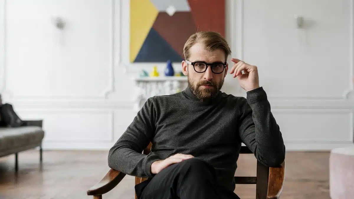 Man with glasses seated in modern interior with abstract art.