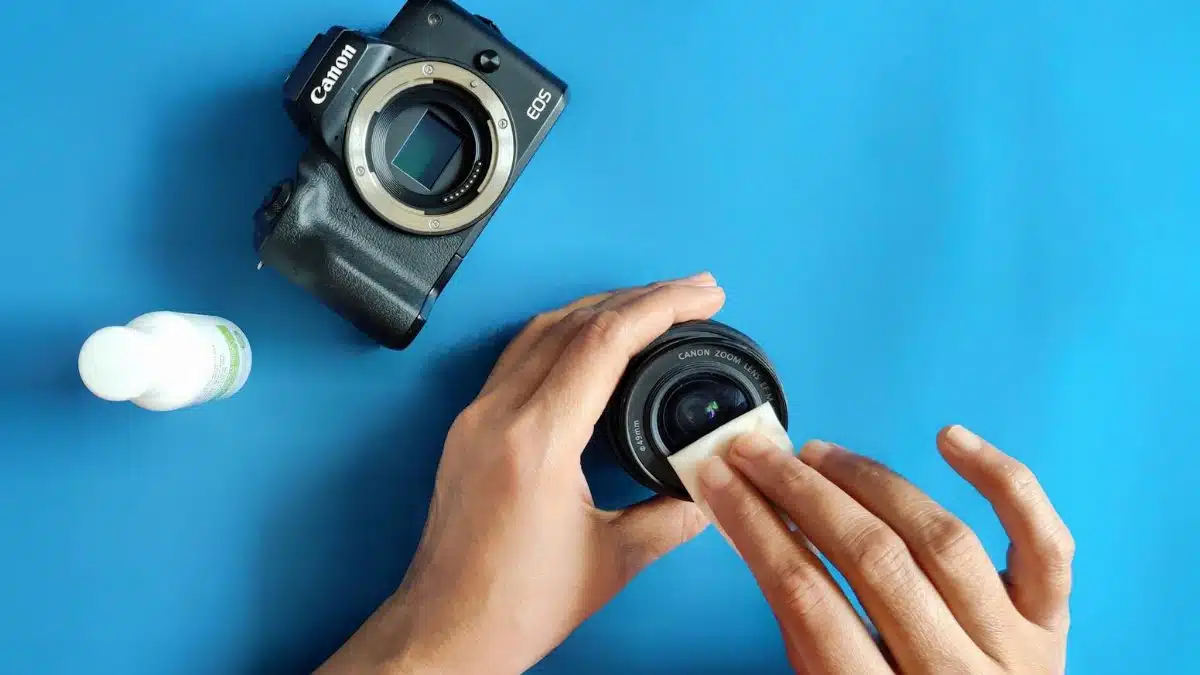 Close-up of hands cleaning a camera lens on a blue surface.