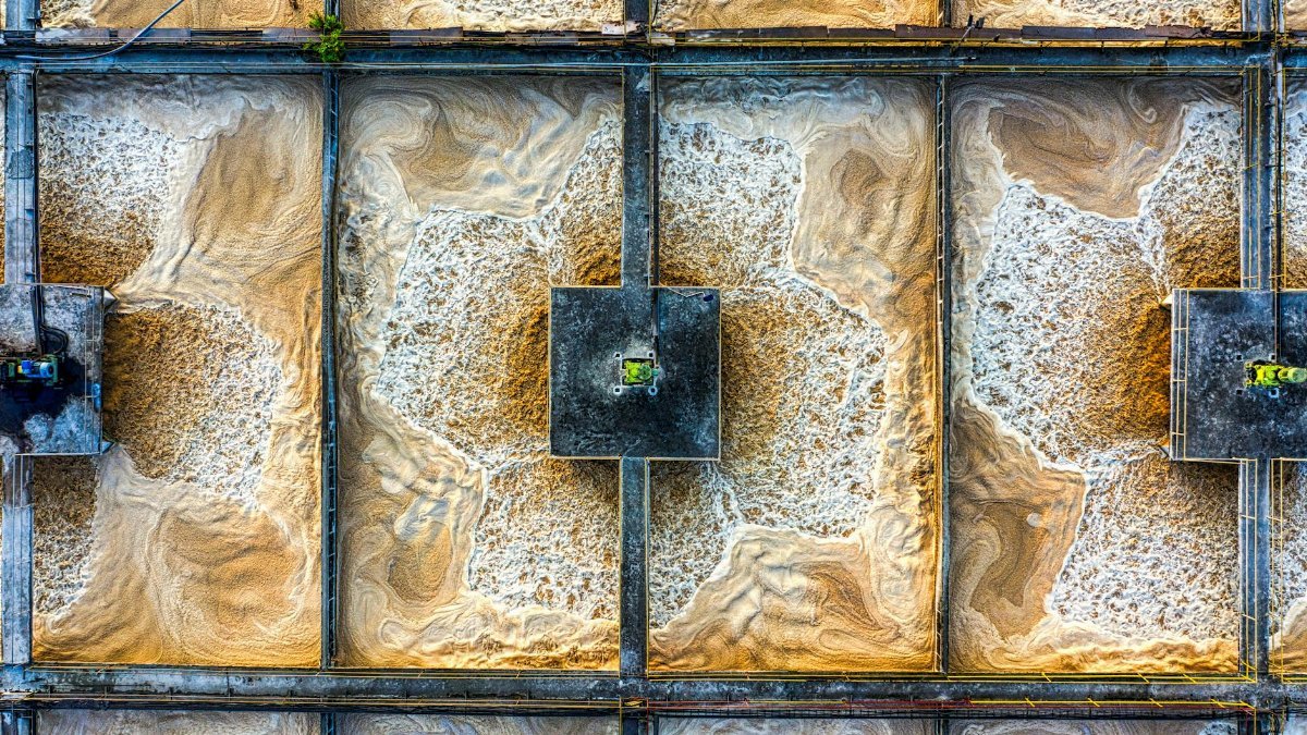 Drone shot of a wastewater treatment plant showcasing intricate grid patterns and swirling water.