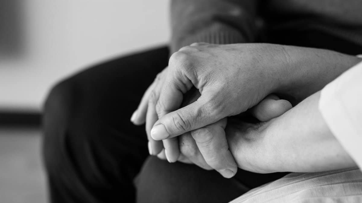 Black and white image of two hands holding, conveying comfort and support, close-up view.