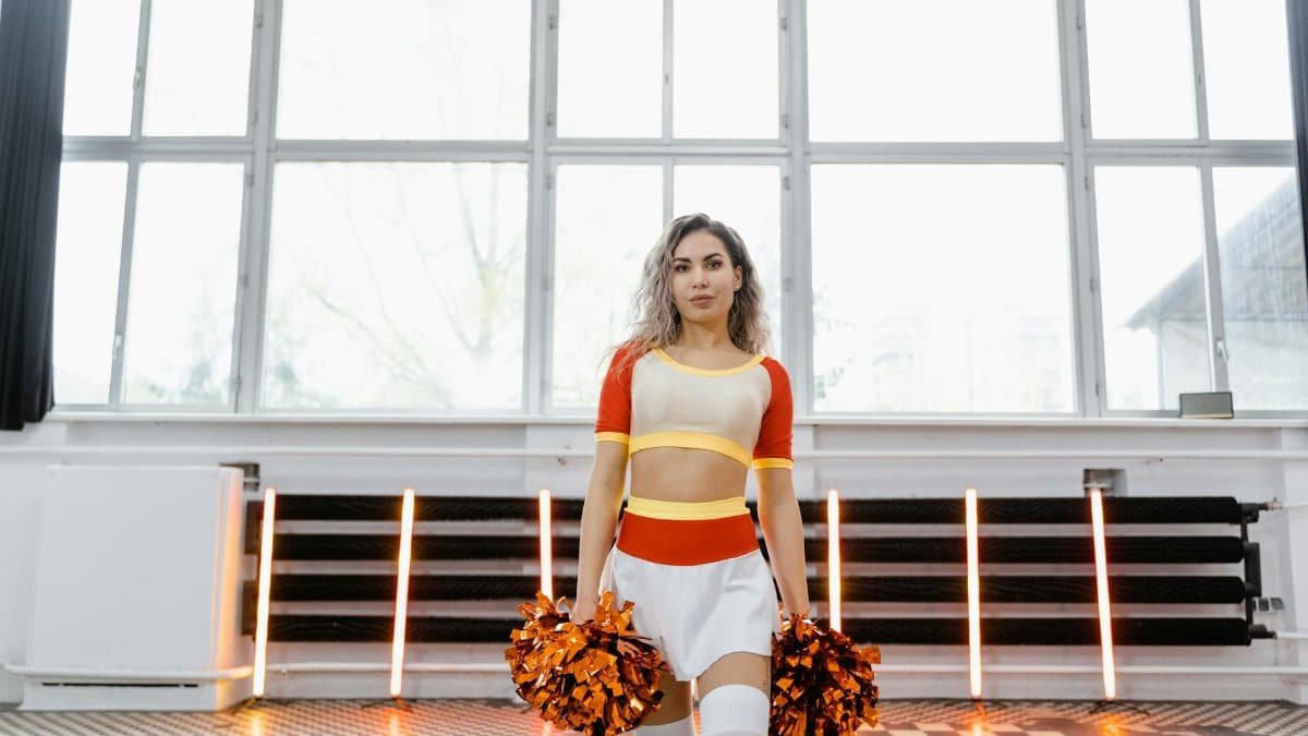 Dynamic image of a cheerleader with pom poms in a bright dance studio setting.