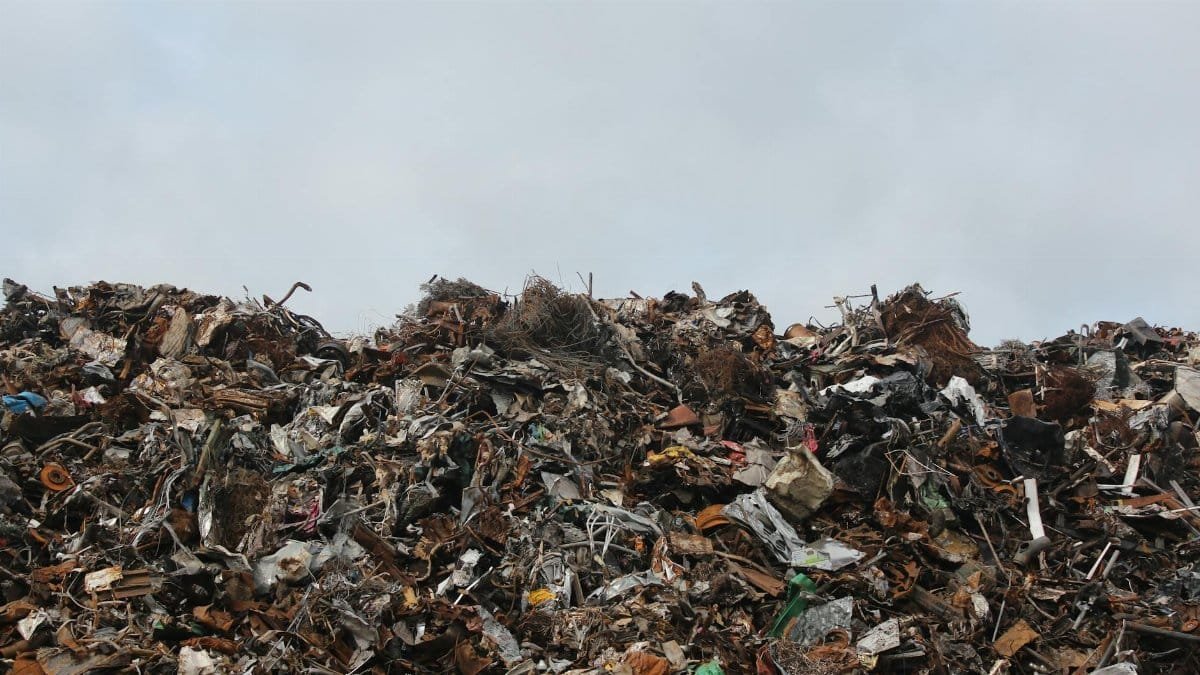 A large pile of scrap metal and waste at a landfill against a cloudy sky.