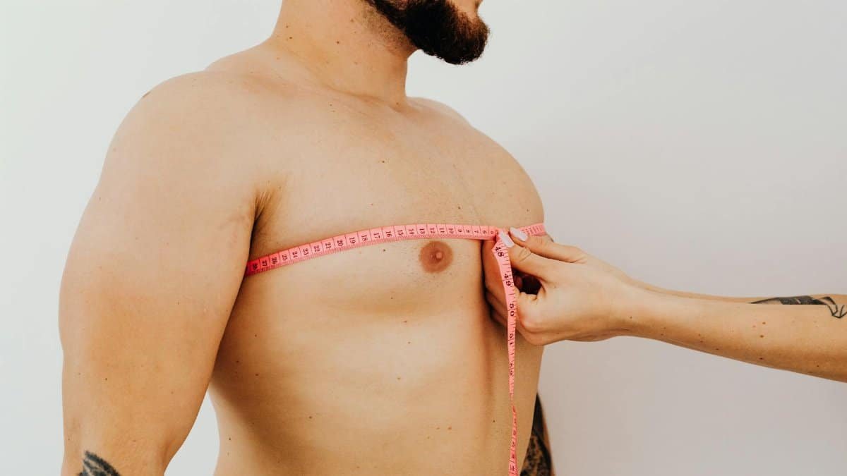 Close-up of a man's chest being measured with a pink measuring tape against a white background.