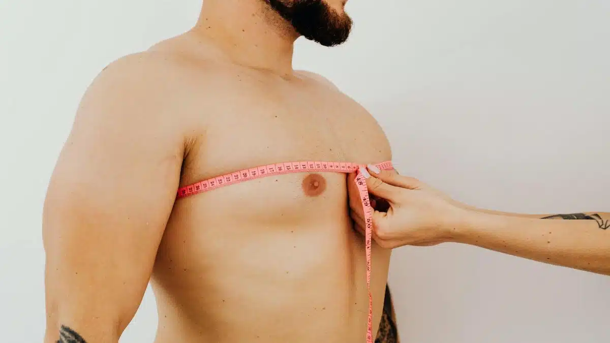 Close-up of a man's chest being measured with a pink measuring tape against a white background.