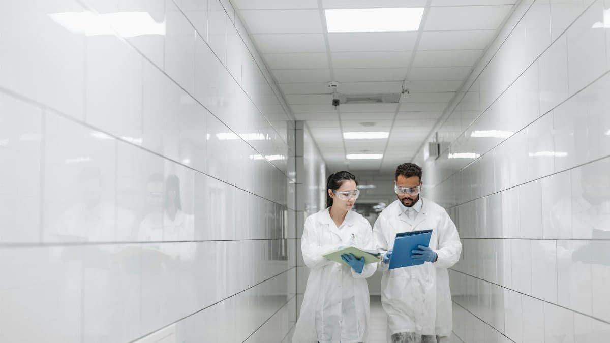 Two medical practitioners in lab coats walking in a clinical hallway discussing paperwork.