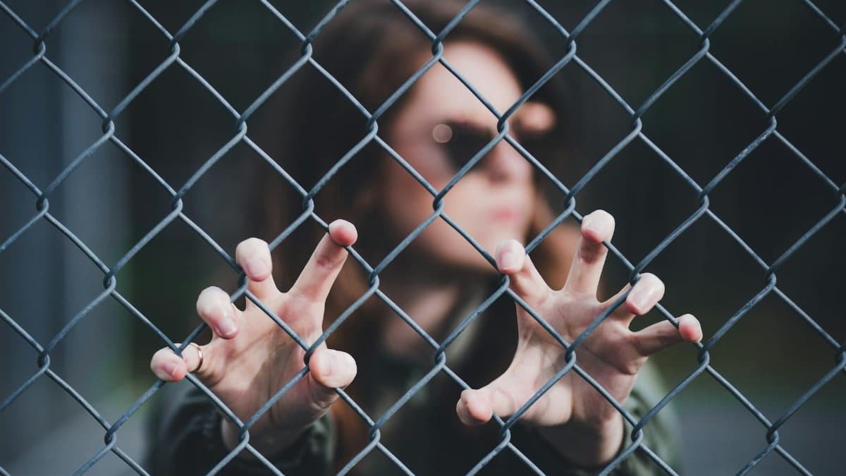 Woman's hands gripping a chain link fence with a focus on introspective mood outdoors.