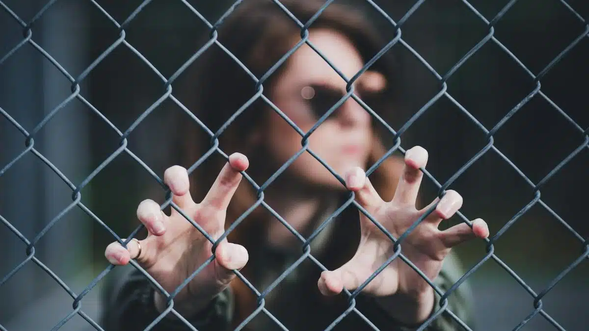 Woman's hands gripping a chain link fence with a focus on introspective mood outdoors.