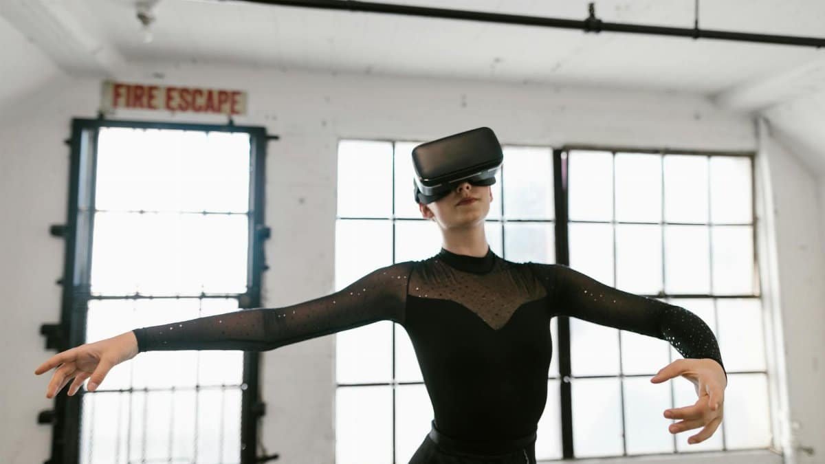 Woman in a black leotard uses virtual reality goggles to perform ballet indoors.