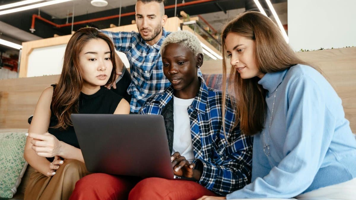 Group of young female and male colleagues checking netbook together in modern workspace in daytime